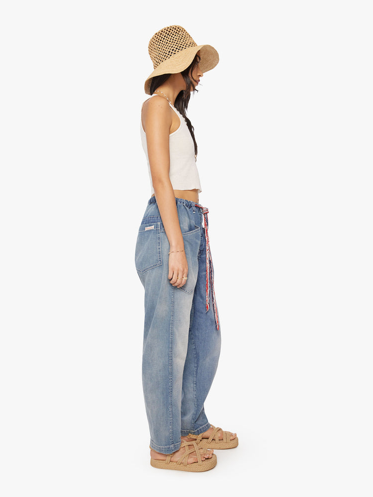 Side view of a woman dark blue wash denim pant with mid rise, narrow straight leg, drawstring waist with a woven belt and a loose fit.