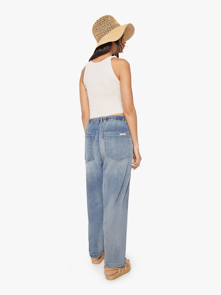 Back view of a woman dark blue wash denim pant with mid rise, narrow straight leg, drawstring waist with a woven belt and a loose fit.