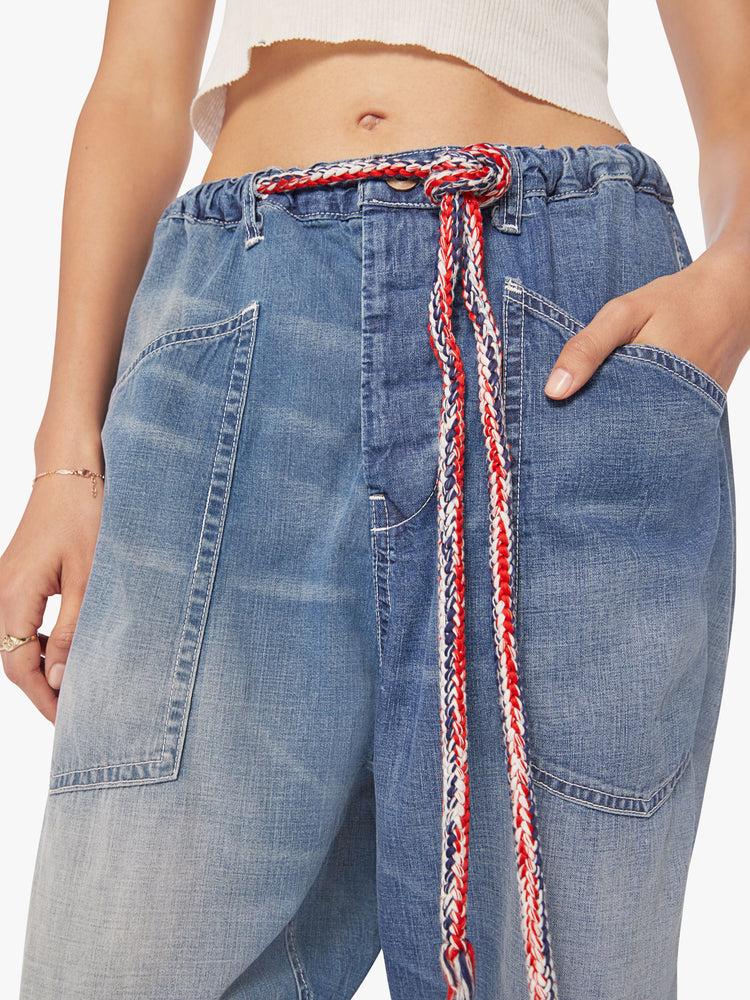 Close up view of a woman dark blue wash denim pant with mid rise, narrow straight leg, drawstring waist with a woven belt and a loose fit.