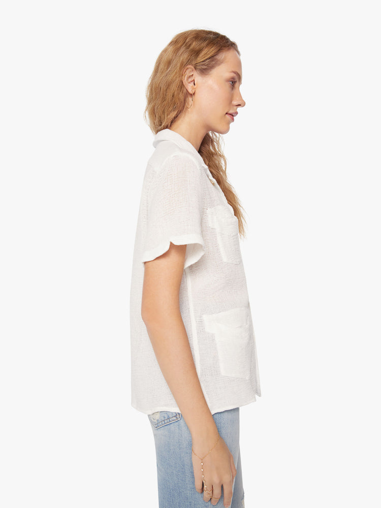 Side view of a woman semi sheer white short-sleeve collared shirt with front patch pockets and boxy fit.