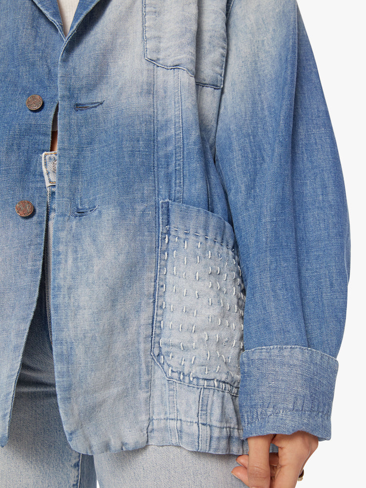 Close up view of a woman denim blazer with a notched collar, front patch pockets, buttons down the front in a vintage blue wash.