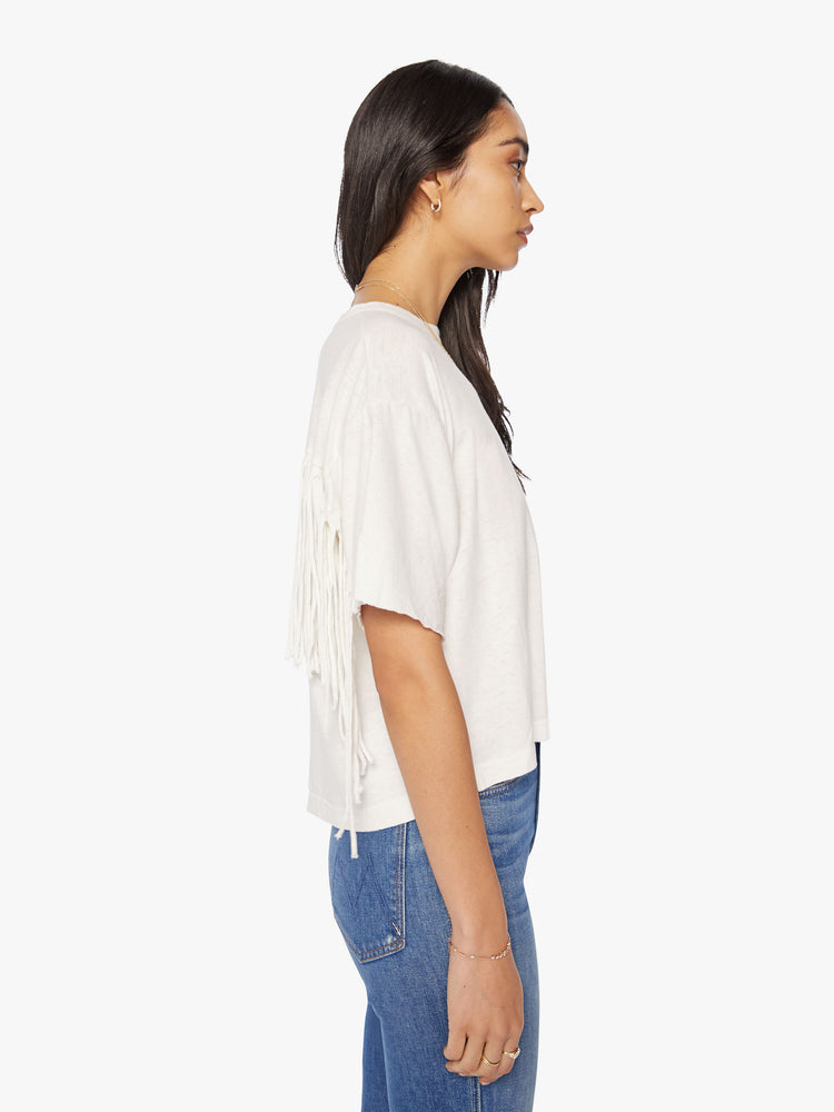Side view of a woman crop tee with drop shoulders, a boxy fit in an off-white hue with fringe across the back.