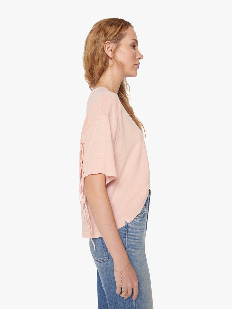 Side view of a woman crop tee with drop shoulders, a boxy fit in a soft pink hue with fringe across the back.