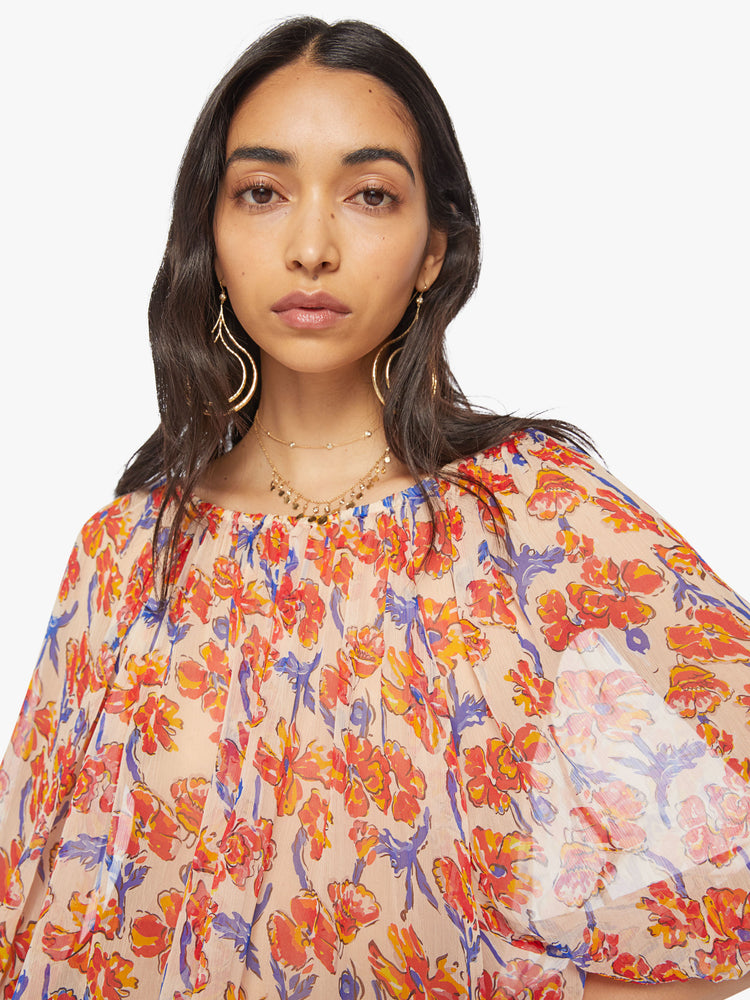 Close up view of a woman's blouse in off-white chiffon with a watercolor floral print in orange and navy and with an elastic boat neck and 3/4-length balloon sleeves.