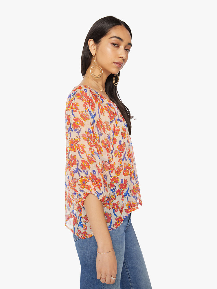 Side view of a woman's blouse in off-white chiffon with a watercolor floral print in orange and navy and with an elastic boat neck and 3/4-length balloon sleeves.
