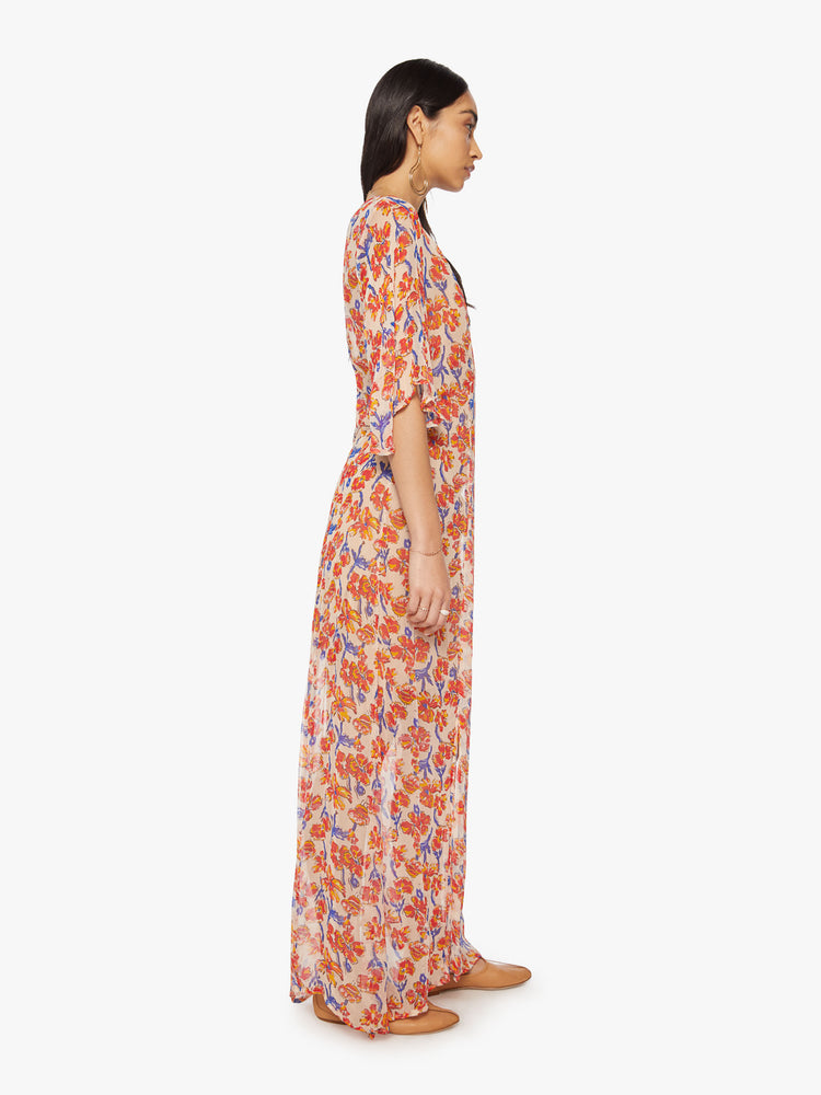 Side view of a woman's maxi dress in an off-white chiffon with a watercolor floral print with a crewneck, elbow-length sleeves, curved waist and ankle length hem.
