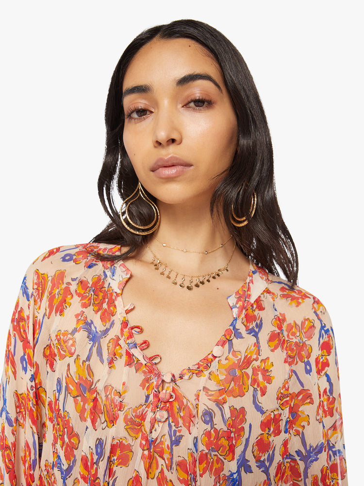 Close up view of a woman's maxi dress in off-white chiffon with a watercolor floral print in orange and navy with voluminous sleeves and has an A-line cut.