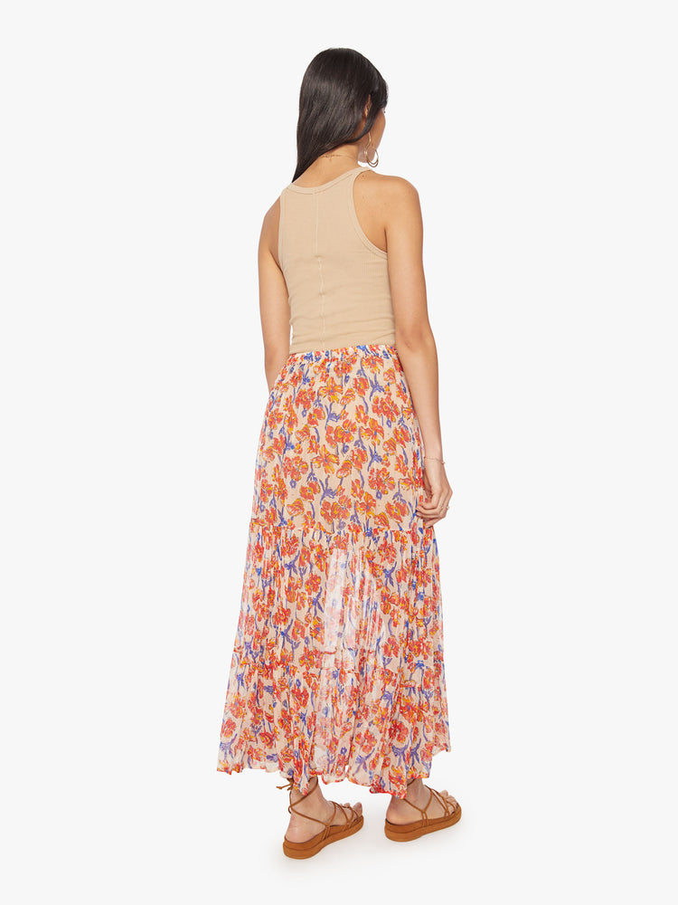 Back view of a woman maxi skirt in an off-white chiffon with a orange/navy watercolor floral print with a drawstring waistband and ruffled hem.