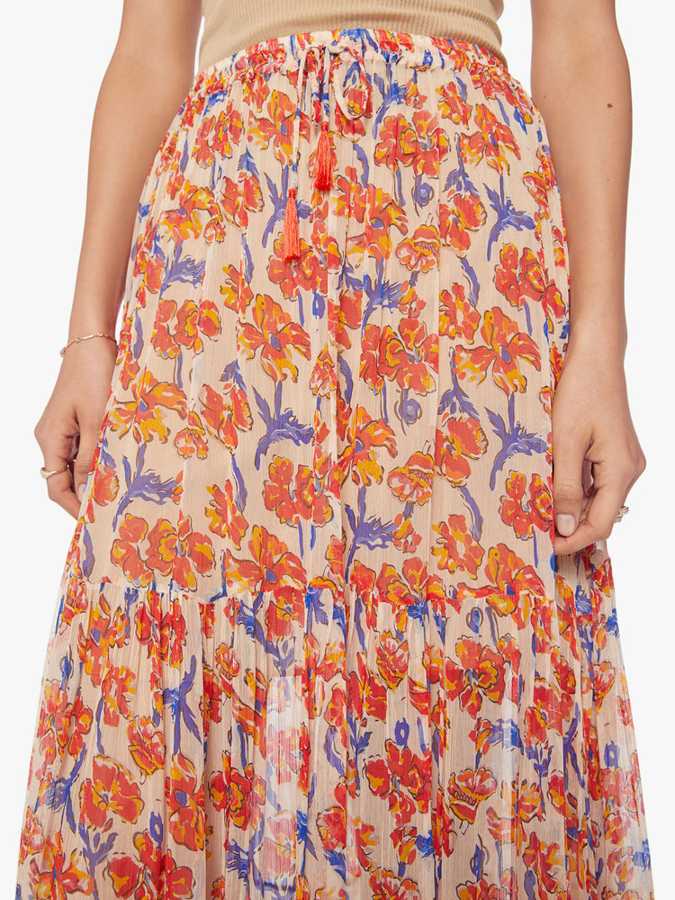 Close up view of a woman maxi skirt in an off-white chiffon with a orange/navy watercolor floral print with a drawstring waistband and ruffled hem.