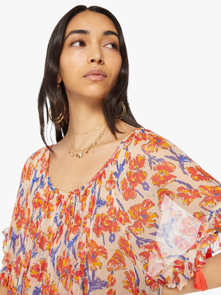 Close up view of a woman dress in an off-white chiffon with a watercolor orange/navy floral print with a wide curved neckline and short balloon sleeves.