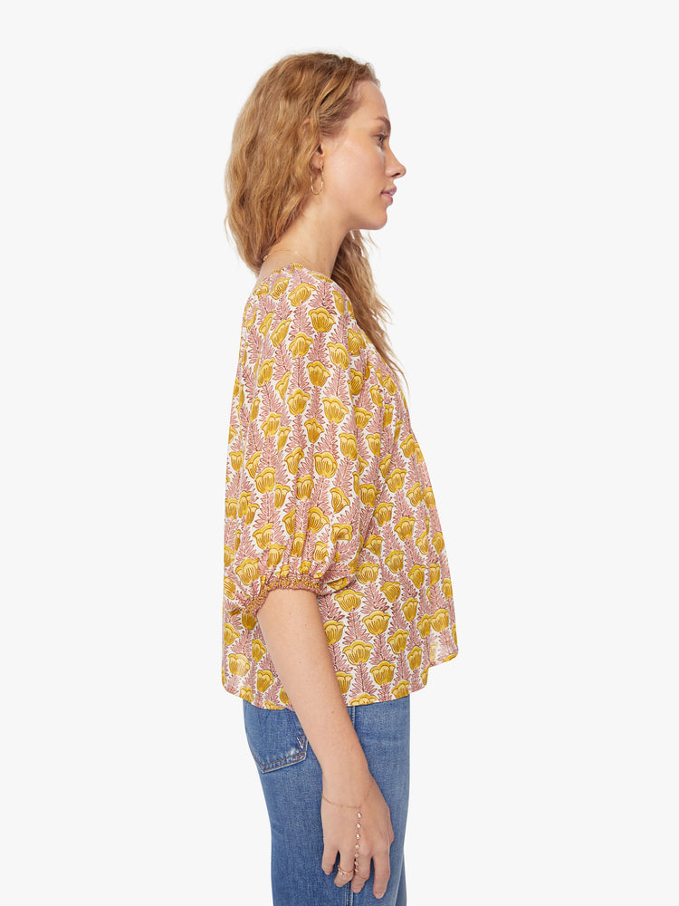 Side view of a woman's blouse in a pink and yellow tulip print and features an elastic boat neck and 3/4-length balloon sleeves.