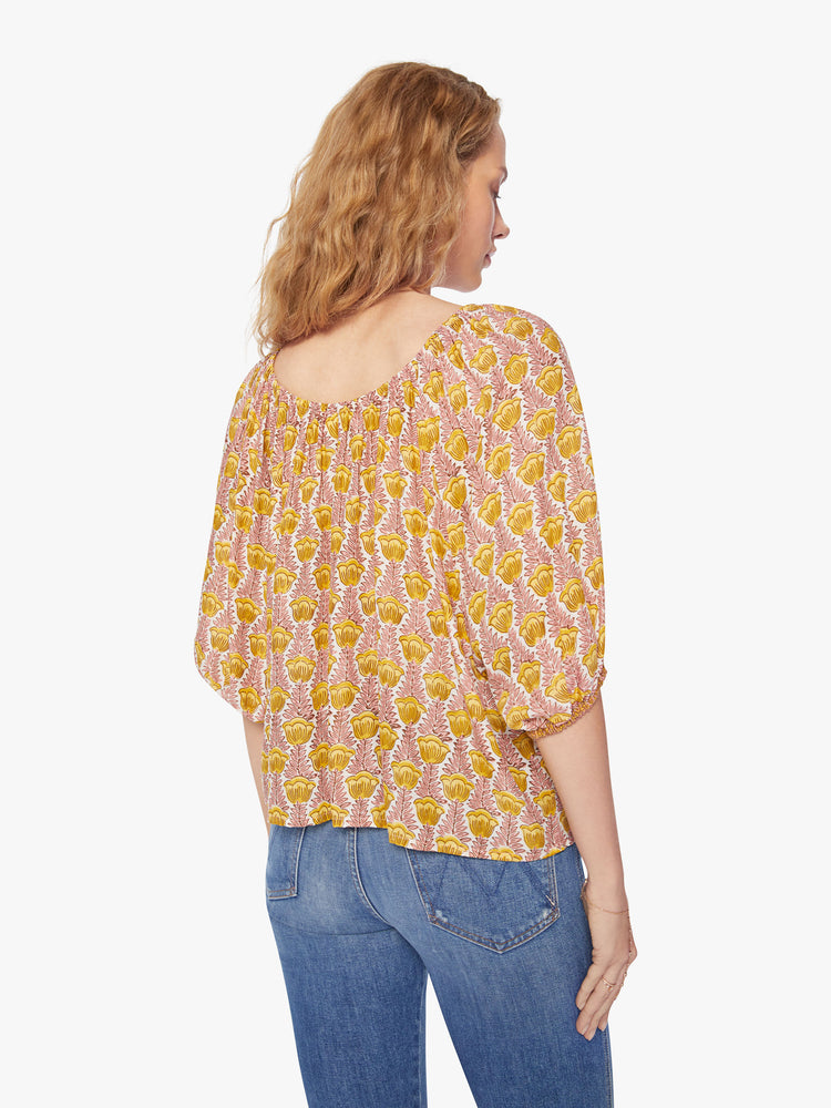 Back view of a woman's blouse in a pink and yellow tulip print and features an elastic boat neck and 3/4-length balloon sleeves.