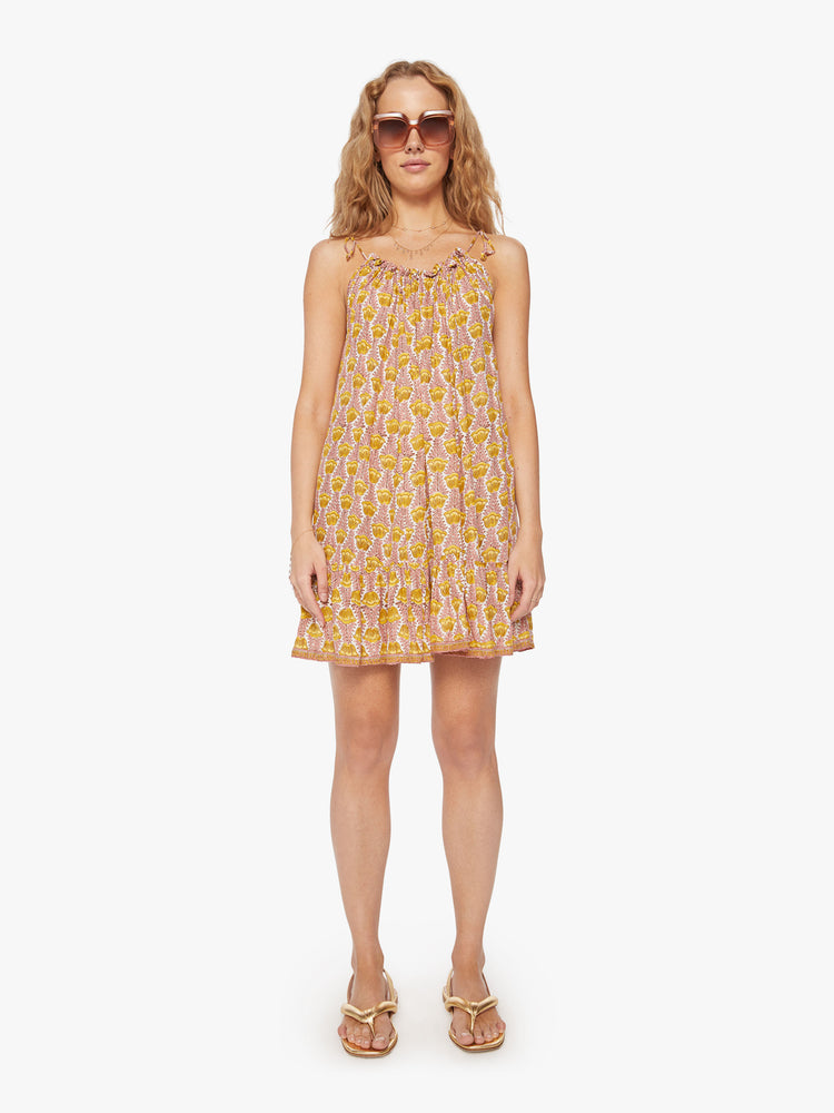 Front view of a woman mini dress in pink and yellow tulip print and a curved neckline, adjustable straps that tie and floaty skirt.