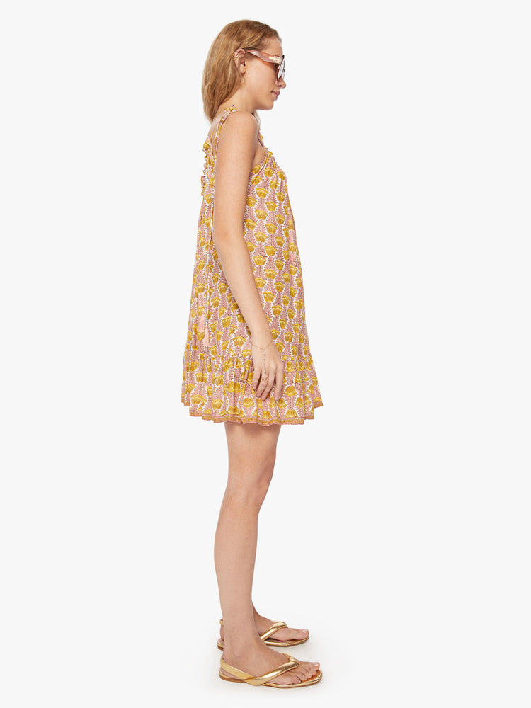 Side view of a woman mini dress in pink and yellow tulip print and a curved neckline, adjustable straps that tie and floaty skirt.