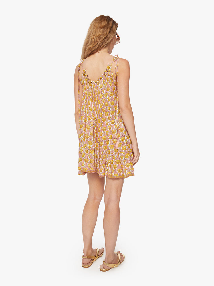 Back view of a woman mini dress in pink and yellow tulip print and a curved neckline, adjustable straps that tie and floaty skirt.