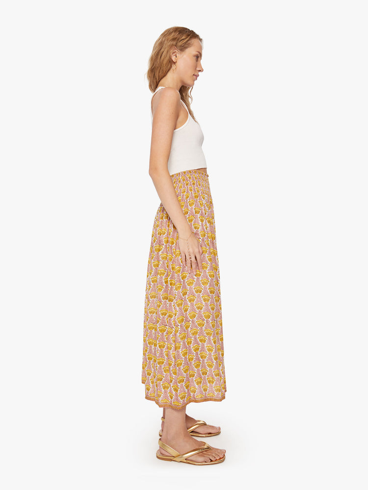 Side view of a woman's maxi skirt in a pink and yellow tulip print and a smocked waistband.
