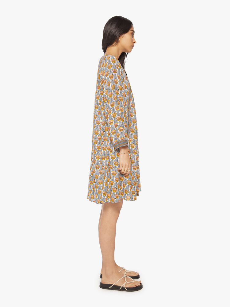 Side view of a woman's maxi dress in blue and yellow tulip print with voluminous sleeves, a deep V-neck with covered buttons.