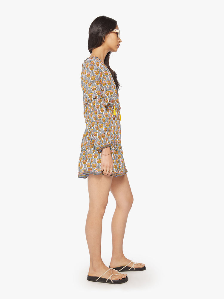 Side view of woman mini dress in a blue and yellow tulip print with a V-neck that ties, long balloon sleeves and mid-thigh tiered skirt.