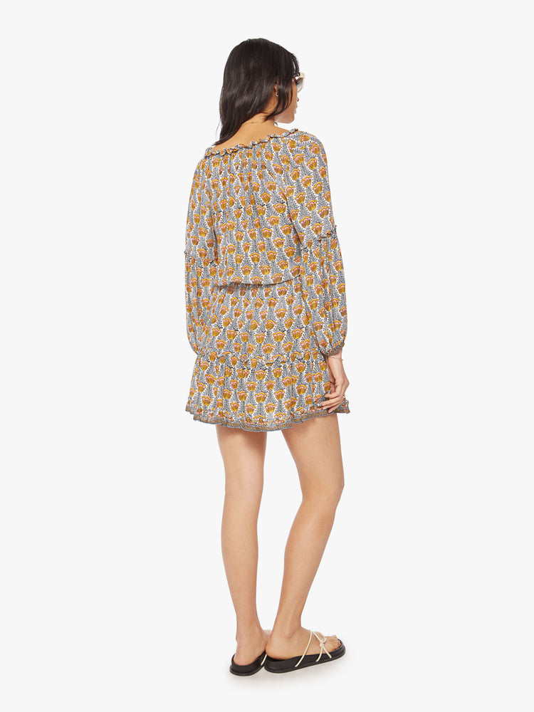 Back view of woman mini dress in a blue and yellow tulip print with a V-neck that ties, long balloon sleeves and mid-thigh tiered skirt.