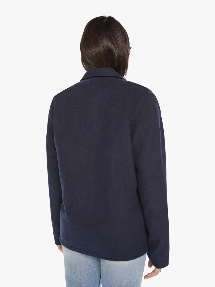 Back view of woman in a dark blue shirt with front patch pockets, long sleeves, buttons down the front and a boxy fit.