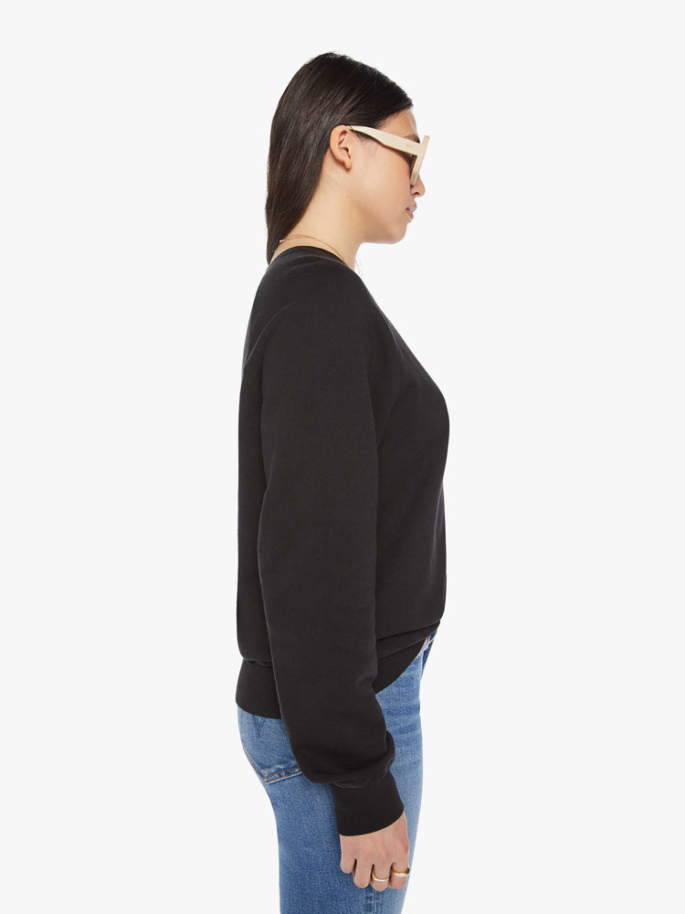 Side view of a woman crewneck sweatshirt with a relaxed shape with raglan sleeves and is decorated with a white club graphic on the back and a logo on the front.