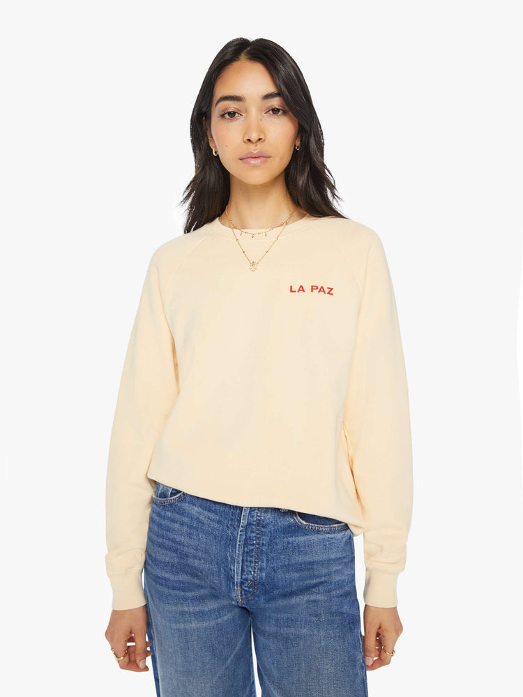 Front view of a woman crewneck sweatshirt in a cream hue with a relaxed shape with raglan sleeves and is decorated with a red diamond graphic on the back and a logo on the front.