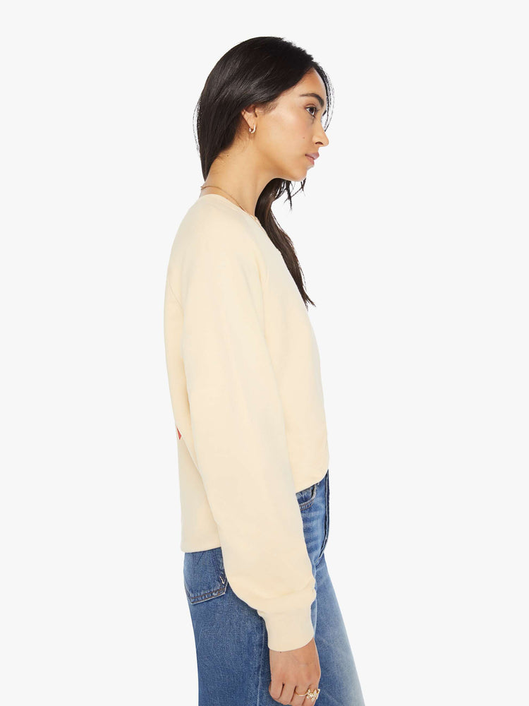 Side view of a woman crewneck sweatshirt in a cream hue with a relaxed shape with raglan sleeves and is decorated with a red diamond graphic on the back and a logo on the front.