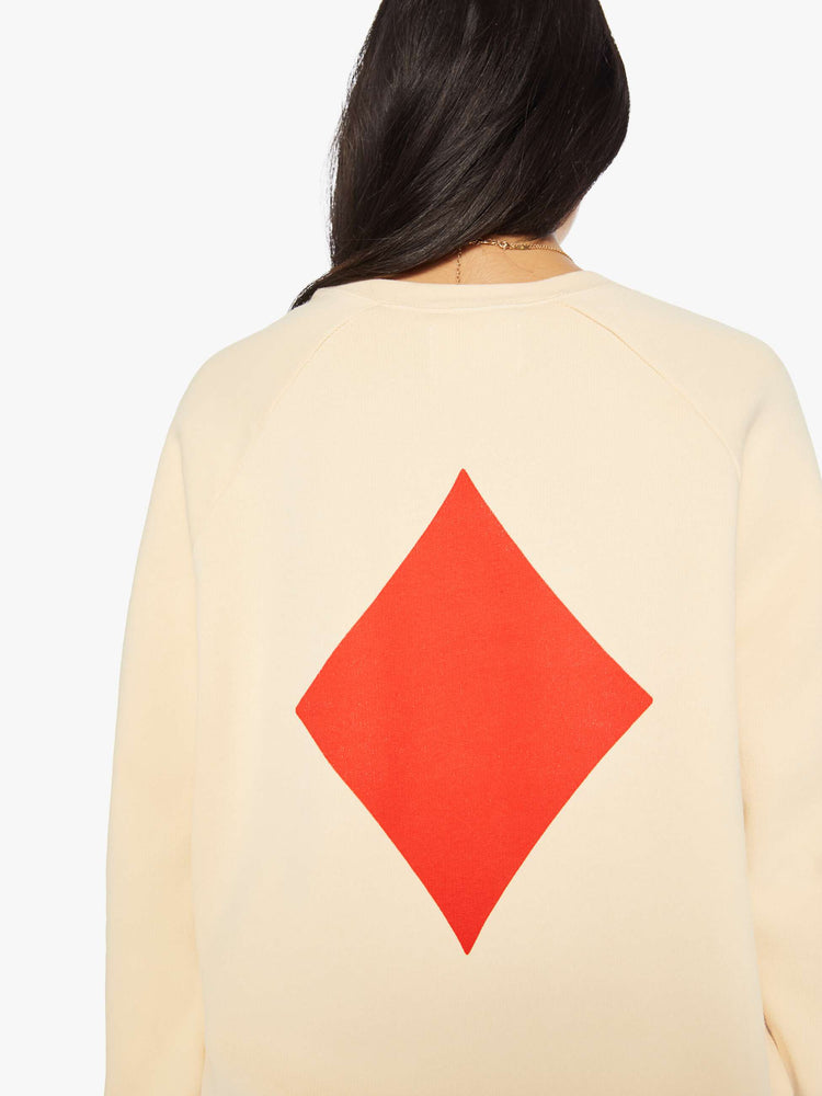 Back close up view of a woman crewneck sweatshirt in a cream hue with a relaxed shape with raglan sleeves and is decorated with a red diamond graphic on the back and a logo on the front.
