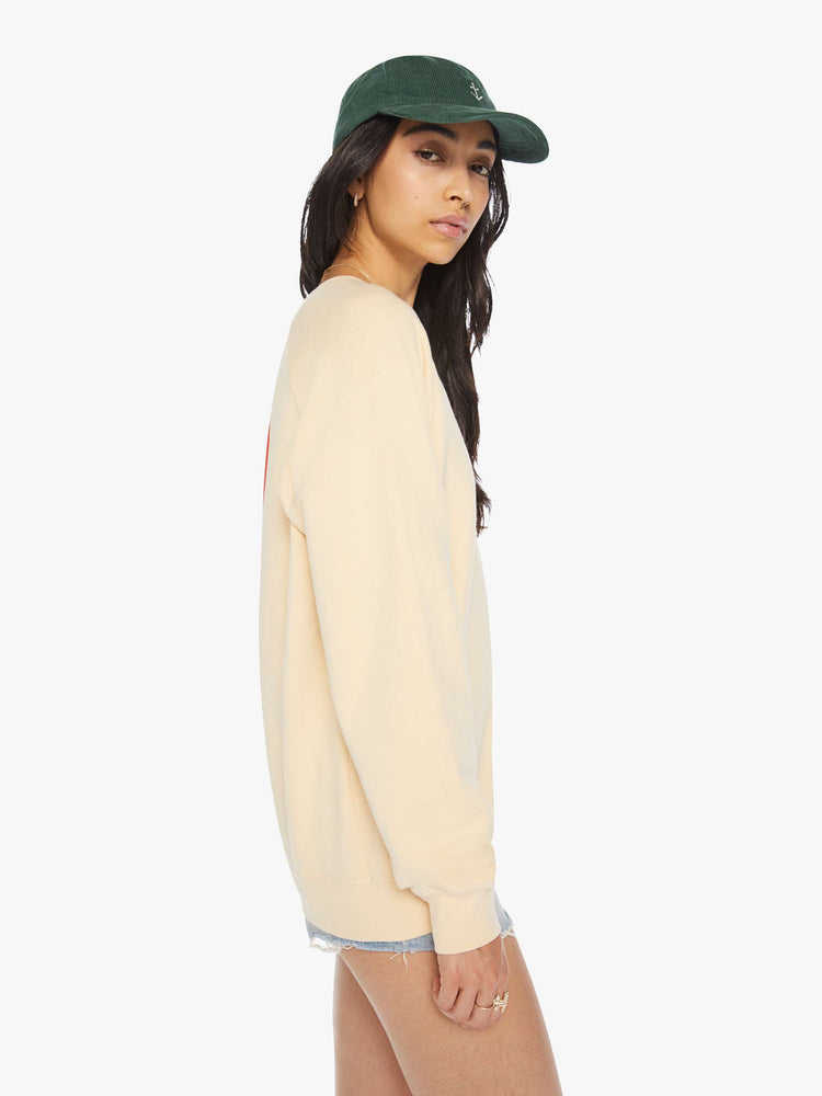 Side view of a woman crewneck sweatshirt in a cream hue with raglan sleeves and is decorated with a red heart graphic on the back and a logo on the front.