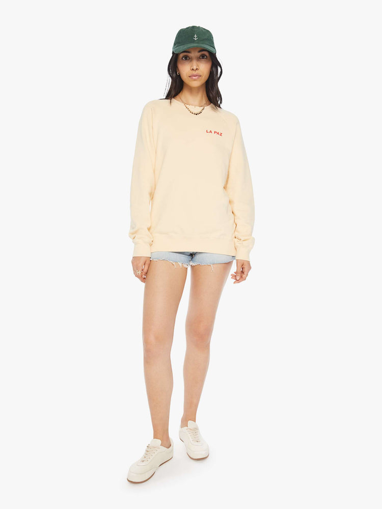 Full body view of a woman crewneck sweatshirt in a cream hue with raglan sleeves and is decorated with a red heart graphic on the back and a logo on the front.