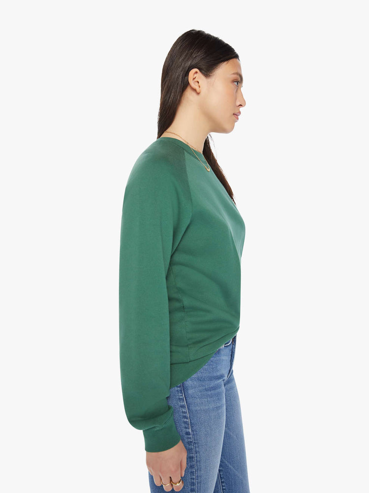 Side view of a woman crewneck sweatshirt in a hunter green hue with a white anchor and has a relaxed shape with raglan sleeves.