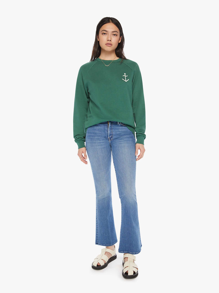 Full body view of a woman crewneck sweatshirt in a hunter green hue with a white anchor and has a relaxed shape with raglan sleeves.