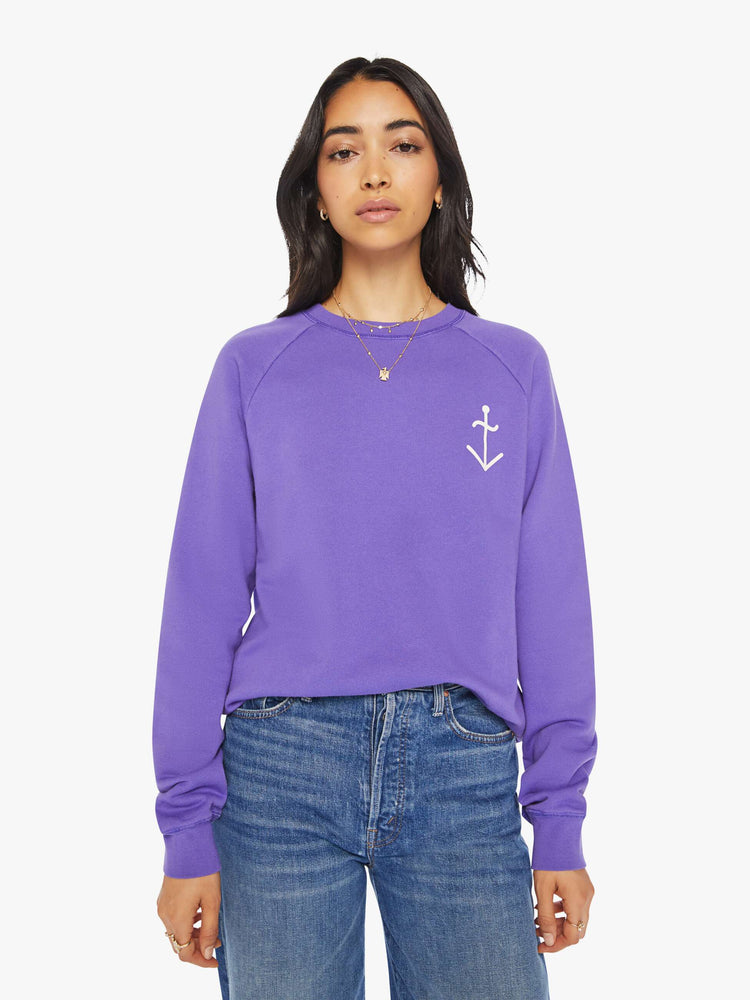 Front view of a woman view of a woman crewneck sweatshirt in a purple hue with a white anchor and has a relaxed shape with raglan sleeves.