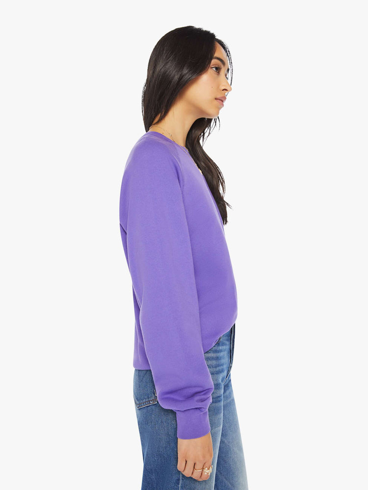 Side view of a woman view of a woman crewneck sweatshirt in a purple hue with a white anchor and has a relaxed shape with raglan sleeves.