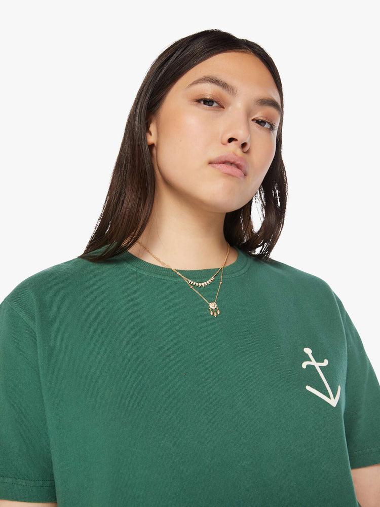 Close up view of a woman green tee with a white anchor on the chest, has a ribbed crewneck and a straight fit.
