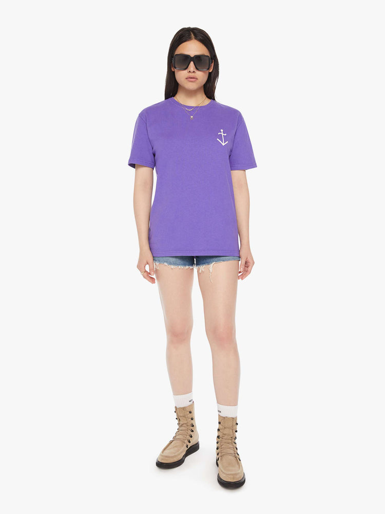 Full body view of a woman purple tee with a white anchor on the chest, has a ribbed crewneck and a straight fit.