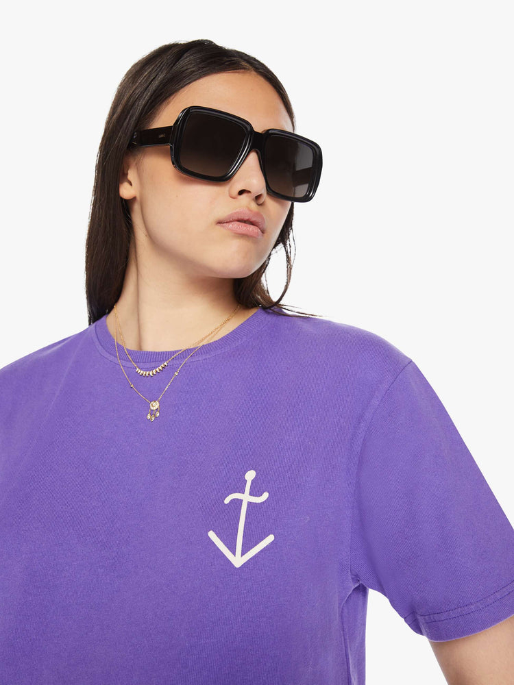 Close up view of a woman purple tee with a white anchor on the chest, has a ribbed crewneck and a straight fit.