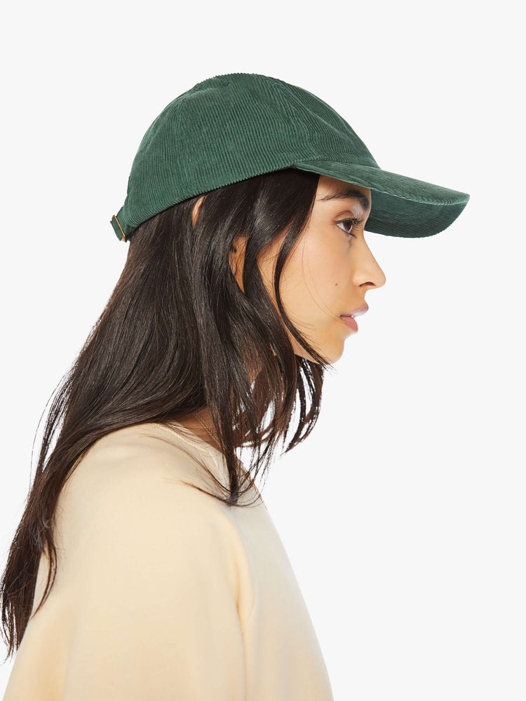 Side view of a woman hunter green hue corduroy hat with a white anchor on the front.