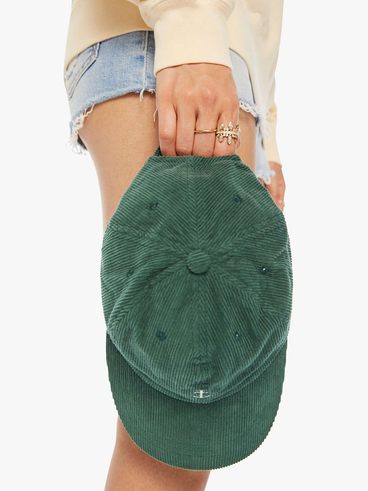 Top close up view of a woman hunter green hue corduroy hat with a white anchor on the front.