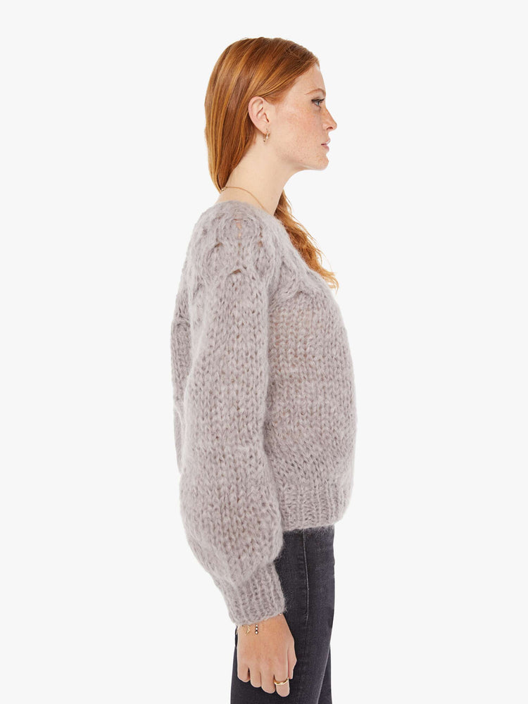 Side view of a womens chunky knit sweater in a grey hue featuring balloon sleeves and ribbed hems.