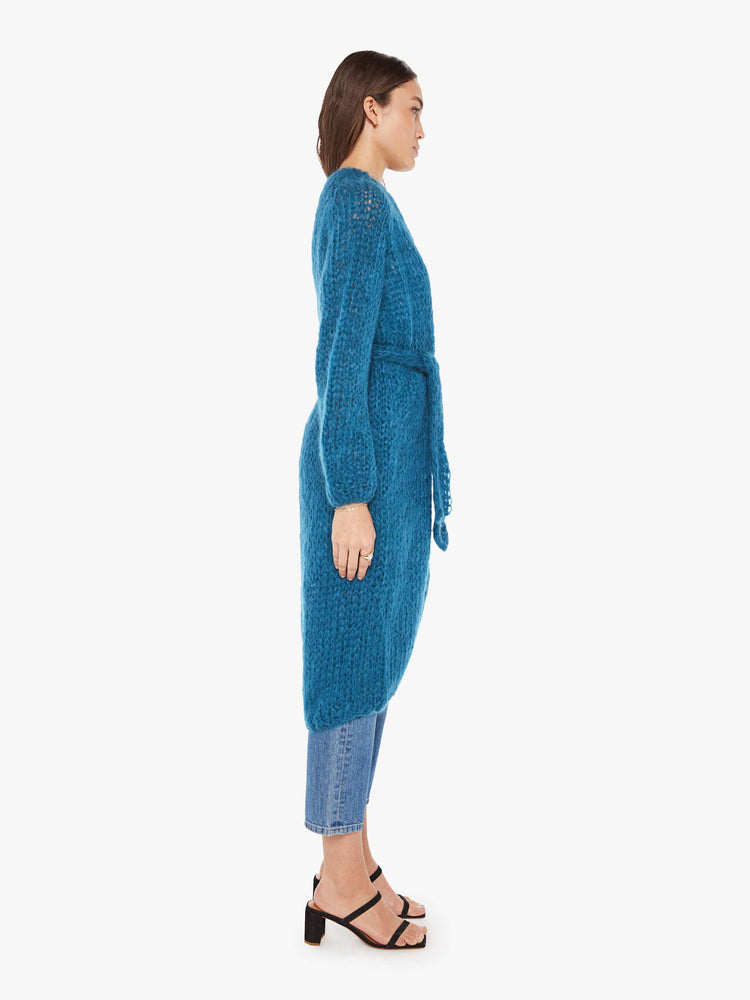 Side view of a womens loose knit blue cardigan coat featuring billow sleeves and a knit belt tie.