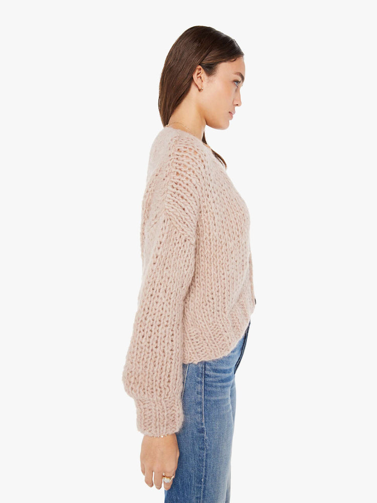 Side view of a womens chunky knit cardigan in a neutral pink hue, featuring a cropped body and three large buttons.