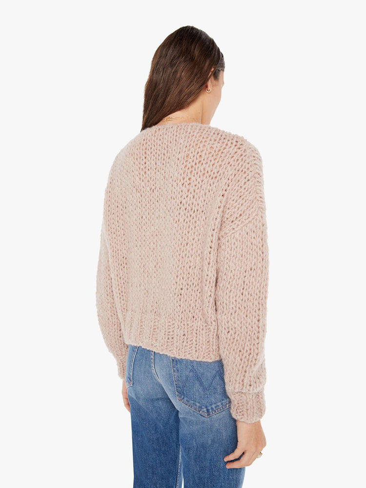 Back view of a womens chunky knit cardigan in a neutral pink hue, featuring a cropped body.