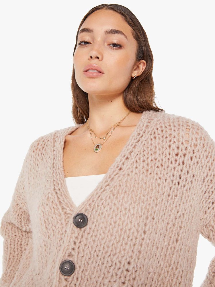 Front close up view of a womens chunky knit cardigan in a neutral pink hue, featuring a cropped body and three large buttons.