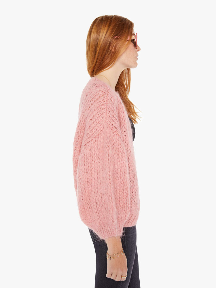 Side view of a womens chunky knit cardigan in a soft pink hue featuring cropped billow sleeves.