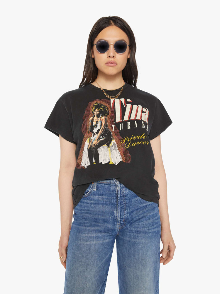 Front view of a woman distressed crewneck tee in black hue , the tee honors Tina Turner, with graphic text and a portrait of the artist on the front.