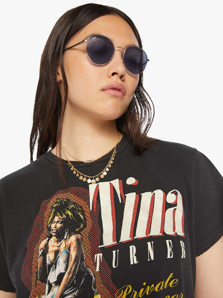 Close up view of a woman distressed crewneck tee in black hue , the tee honors Tina Turner, with graphic text and a portrait of the artist on the front.