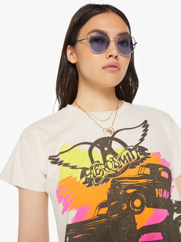 Front close up view of a woman distressed crewneck tee in white, the tee riffs on Aerosmith merch from 1990 with neon graphics and bold text on the front and back.