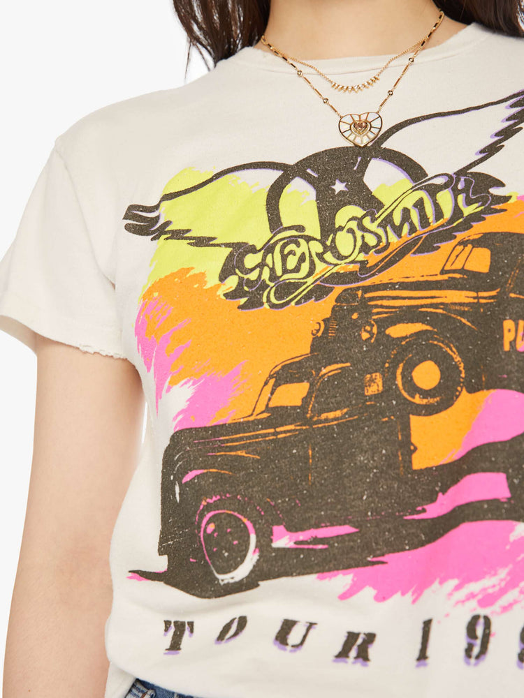 Close up view of a woman distressed crewneck tee in white, the tee riffs on Aerosmith merch from 1990 with neon graphics and bold text on the front and back.