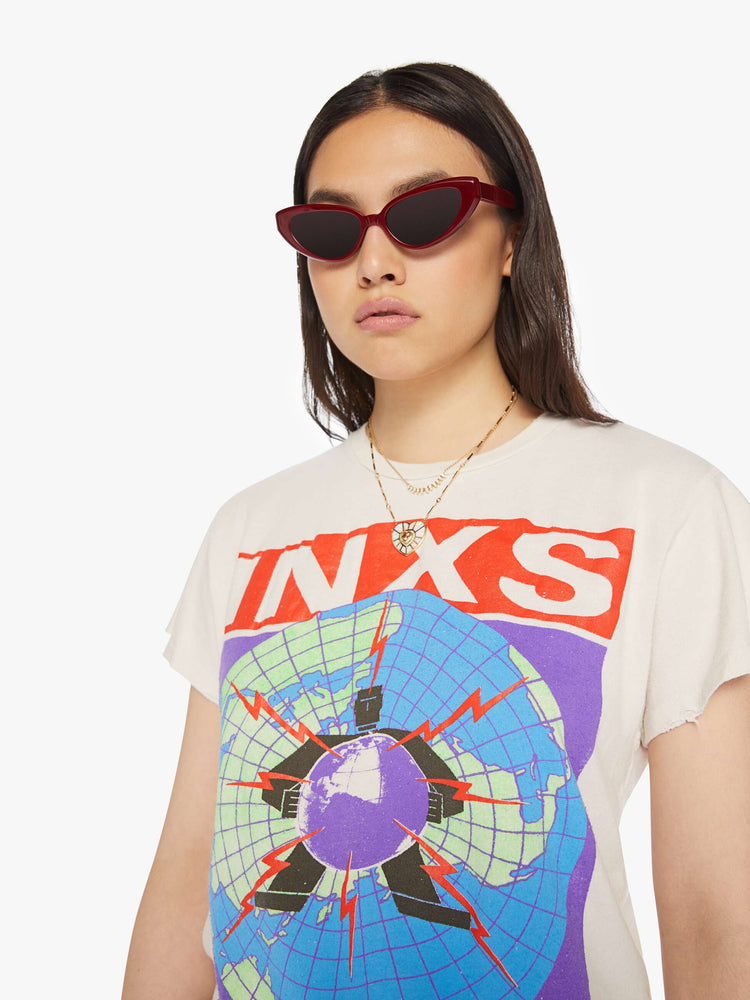 Close up view of a woman distressed crewneck tee in white, the tee pays homage to INXS' Calling All Nations tour with bold graphics on the front and back. 